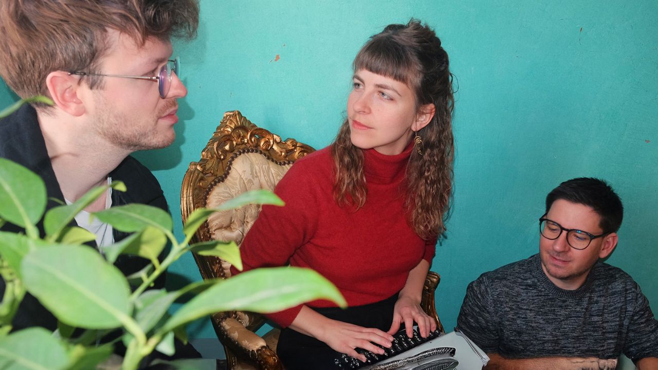 eine Frau zwei Männer mit Zimmerpflanze und Schreibmaschine