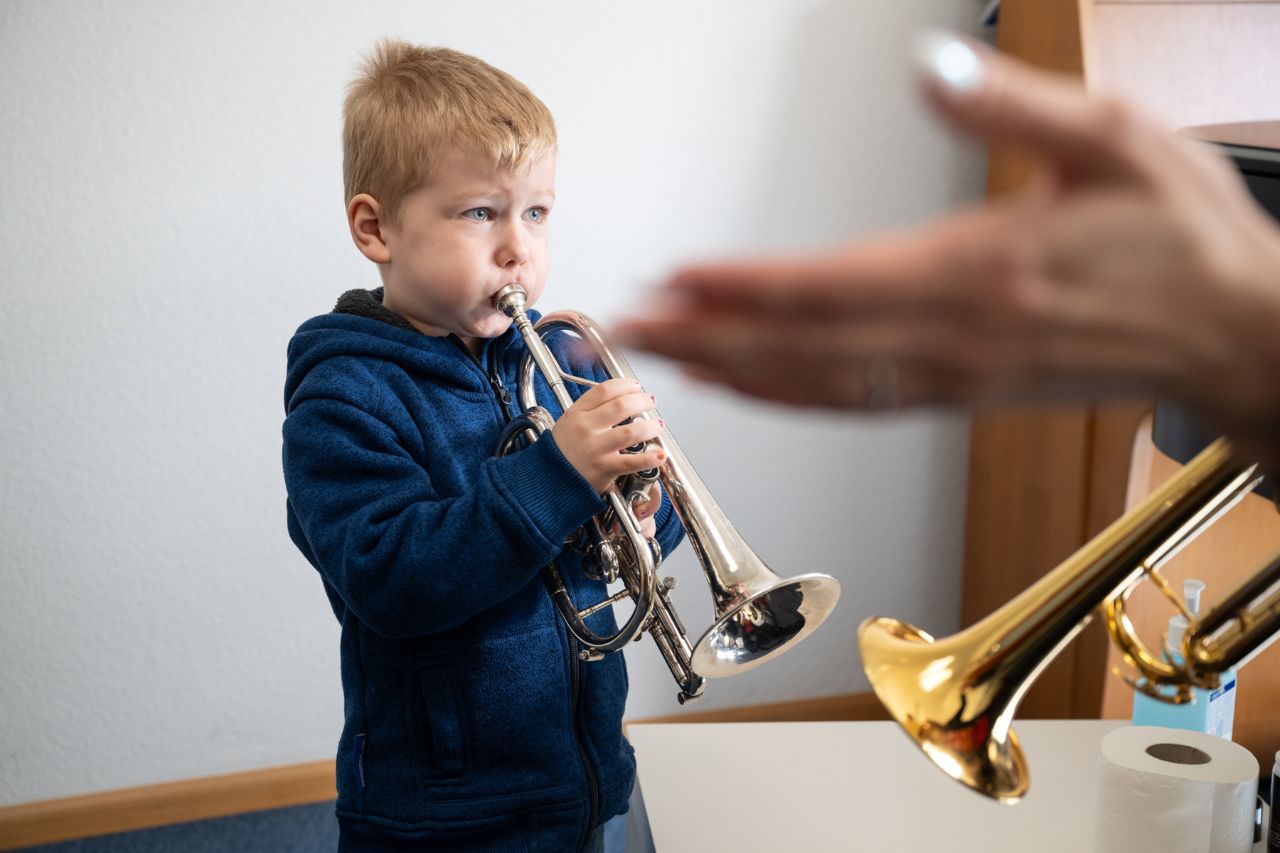 Ein Kind mit kurzen, blonden Haaren spielt Trompete. 